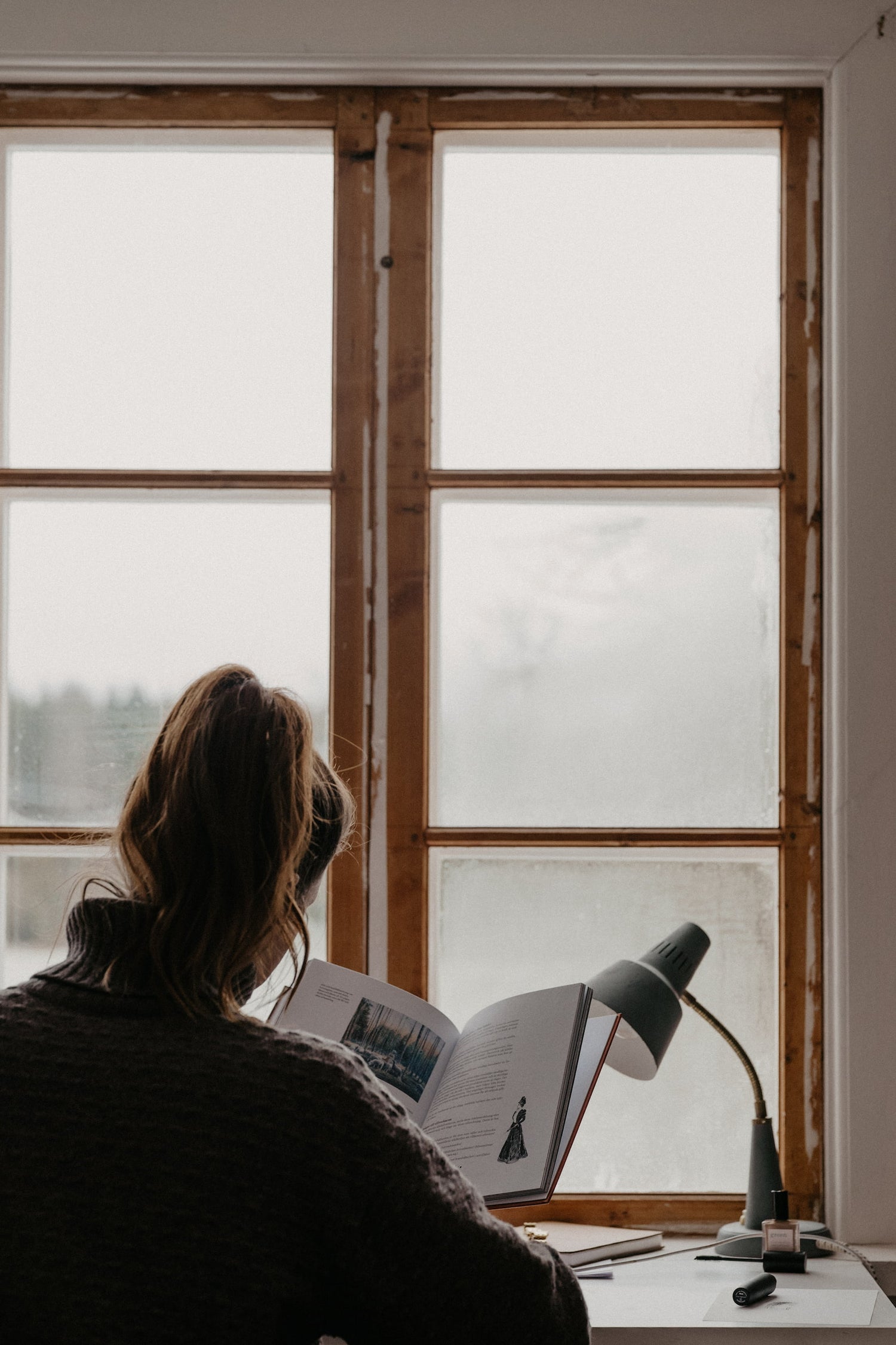 en tjej läser en bok framför ett fönster
