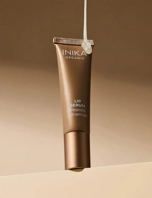 INIKA Tinted Lip Serum i guldfärgad tub mot beige bakgrund